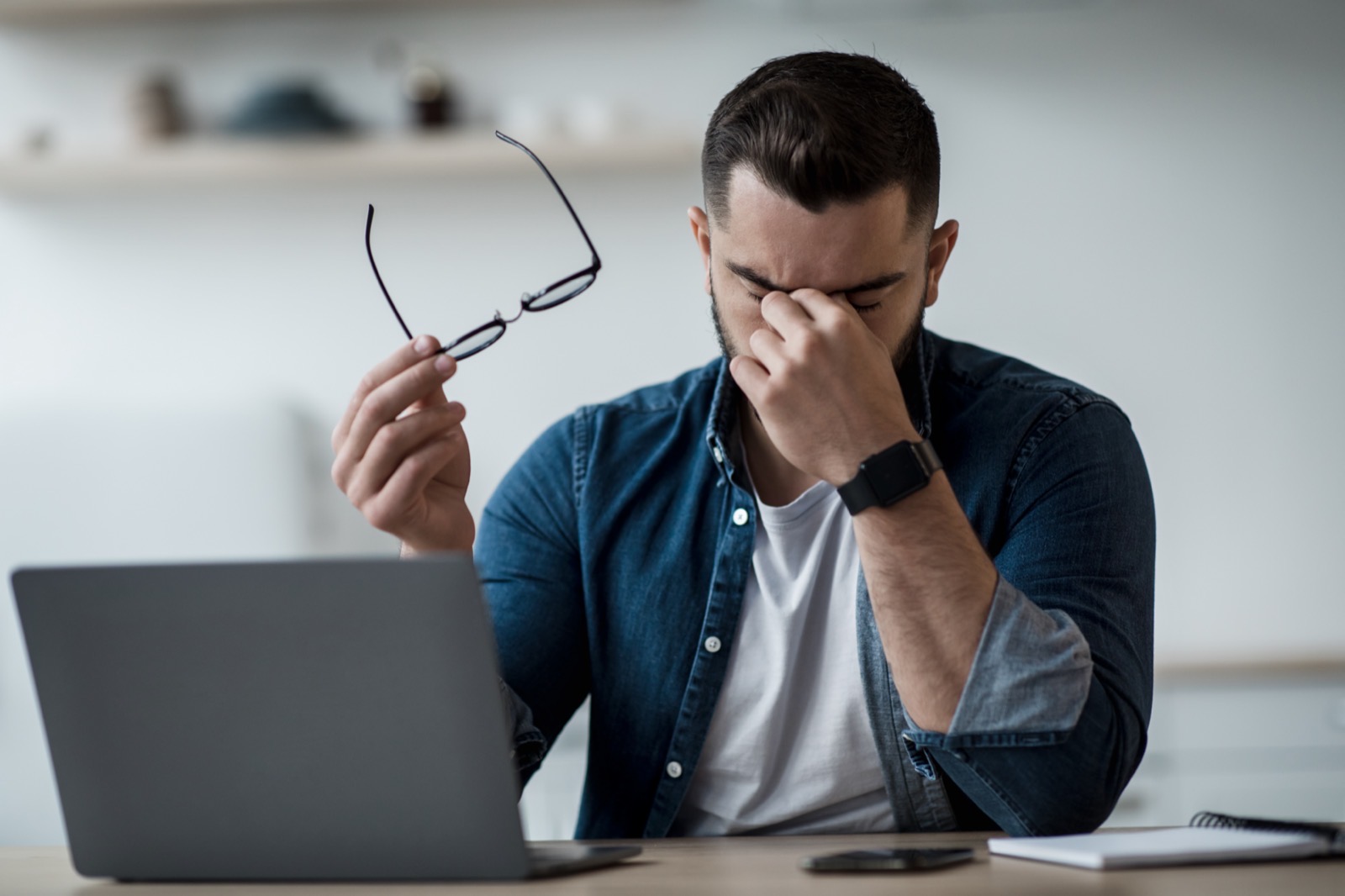 Man rubbing his tired eyes while working at a laptop — a common dry eye symptom